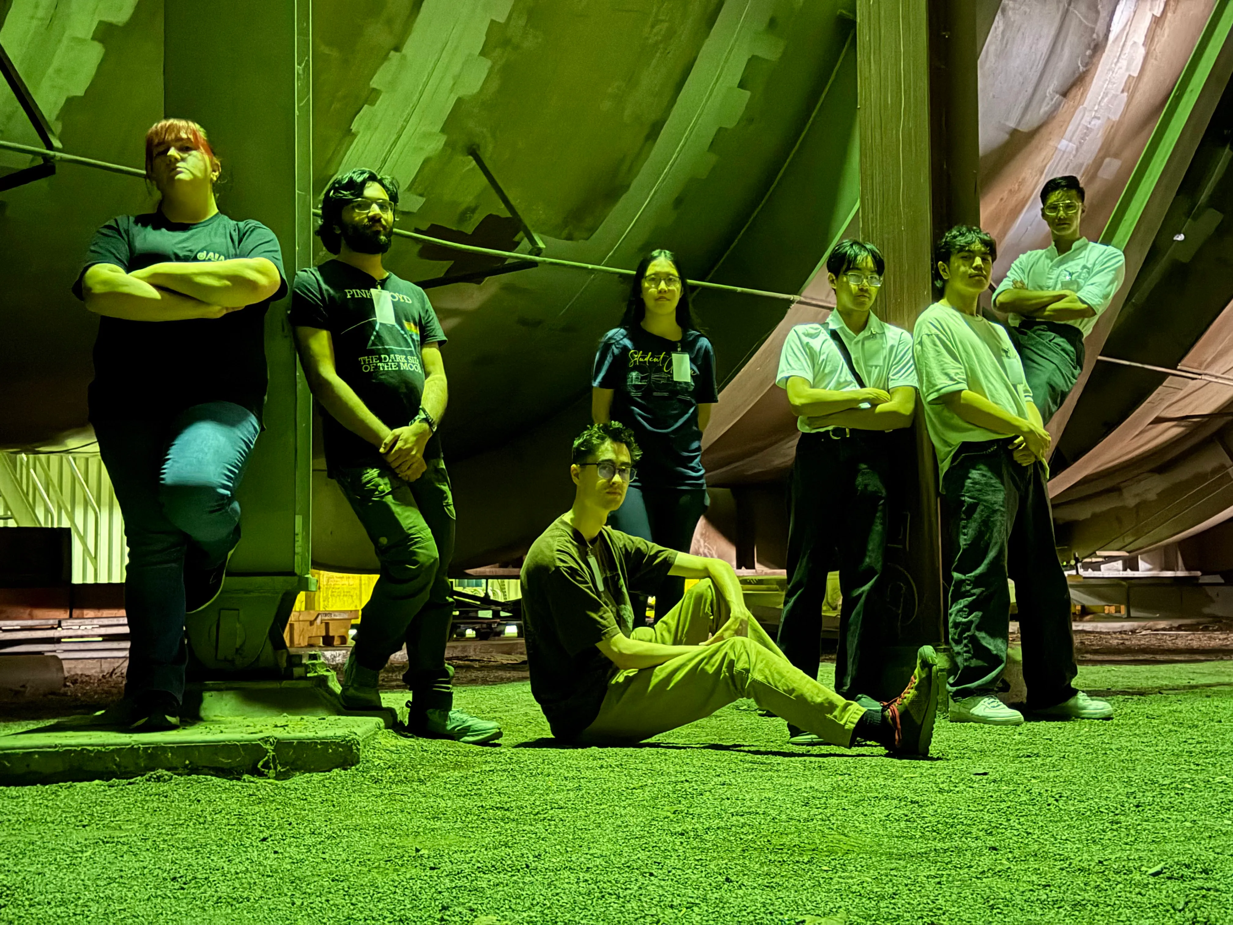 Seven people posing in front of a massive metallic cylinder that is part of the NASA Ames Unitary Plan Wind Tunnel.